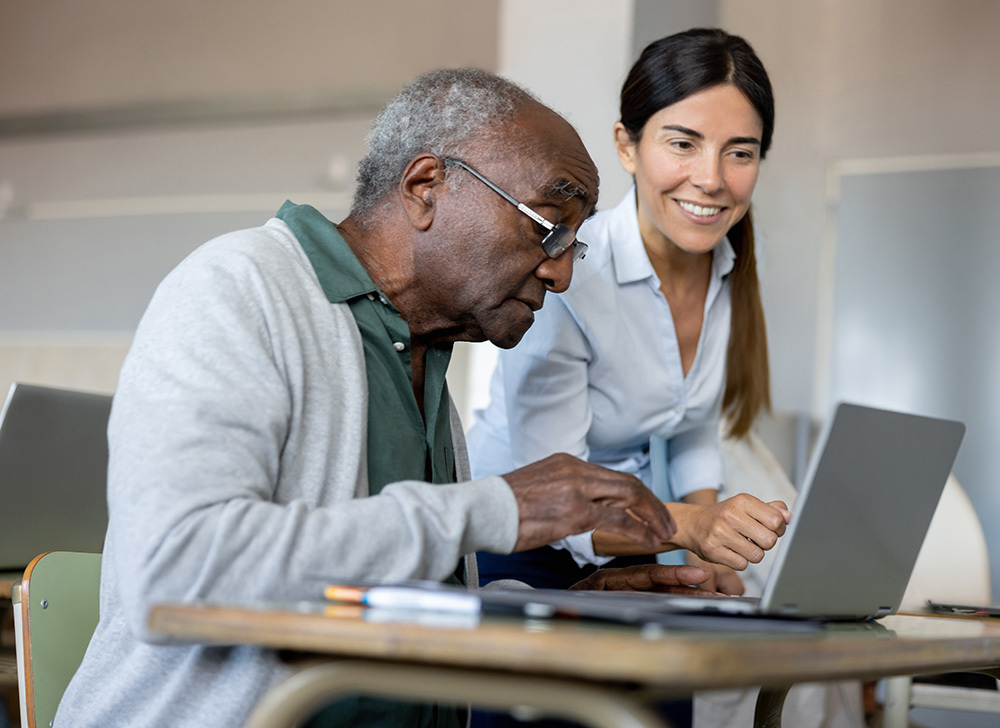 young woman teaching elderly to use computer
